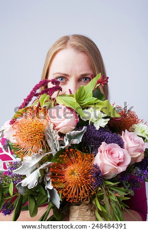 Blond female holding a large bunch of flowers in front of her face
