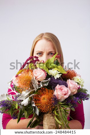 Blond female holding a large bunch of flowers in front of her face
