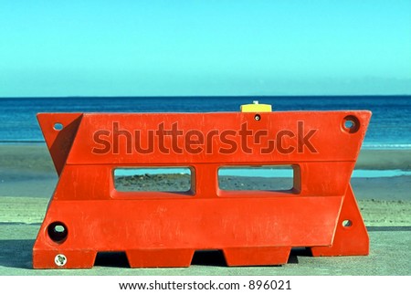 Large red, water filled plastic road barrier, near the beach