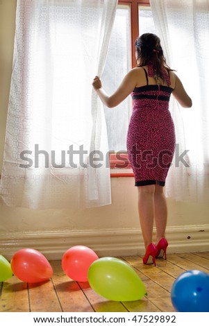 Girl in pink dress and high heeled shoes looking through curtains with balloons on the floor