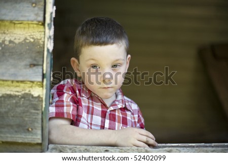 Serious looking six year old boy looking out a farmhouse window frame