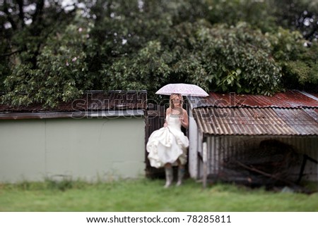 Beautiful young bride in her wedding dress, stands in the rain with colorful Umbrella
