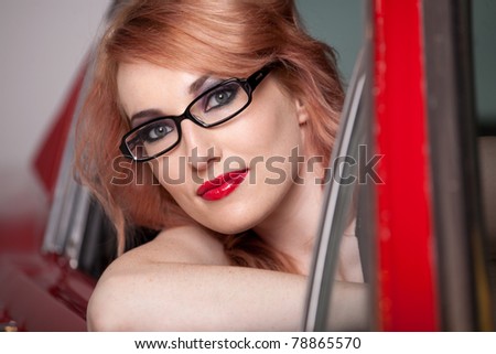 Beautiful Woman with Red hair and wearing black rim glasses sitting in red car