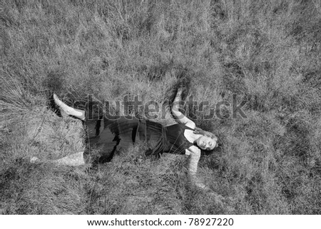Aerial view of girl in long dress lying on her back in field of long grass