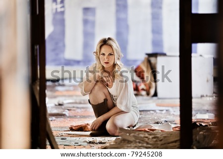 A beautiful woman with blond hair kneeling down in a abandoned derelict building