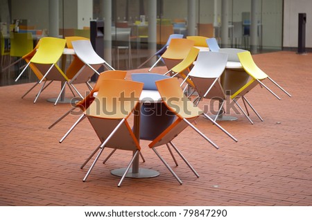 Colorful plastic and aluminum chairs leaning against tables at a cafe outdoor dining area