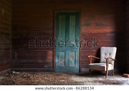 A beautiful old armchair left inside an abandoned home with red timber walls and a green door