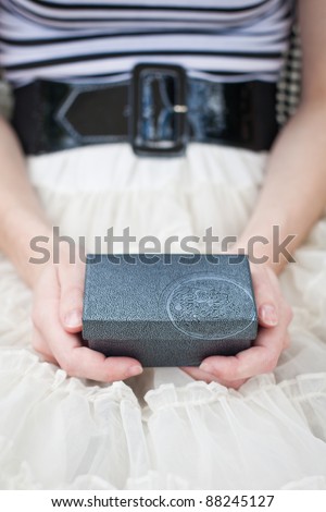 A beautiful young woman wearing a lace skirt sits with a Gift Box in her hands on her lap