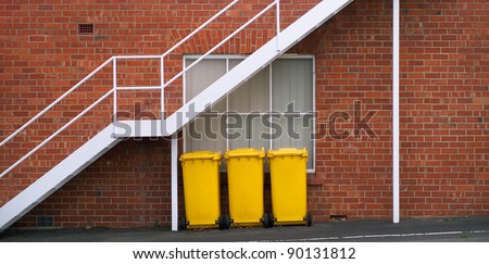 Three large bright yellow plastic rubbish bins outside a building
