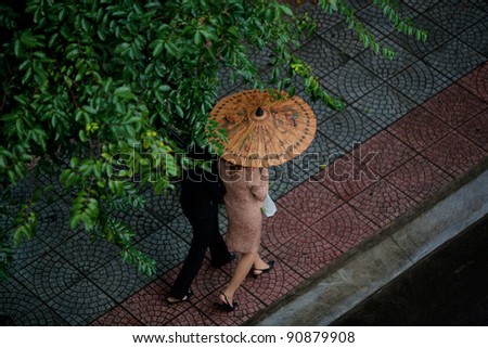 Two people walking in the rain sheltering under a bamboo Umbrella on the streets of Saigon(Ho Chi Min City), Vietnam