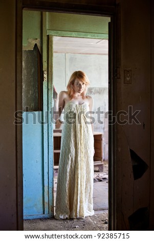 Beautiful redhead woman wearing long flowing dress standing in derelict abandoned house