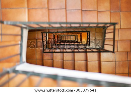 Looking down internal staircase in apartment building, with tiled steps and metal hand rails
