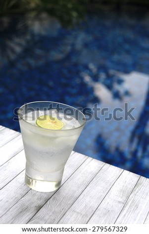A glass of iced coconut water, garnished with lime slice. Placed on rustic wooden board by the pool.