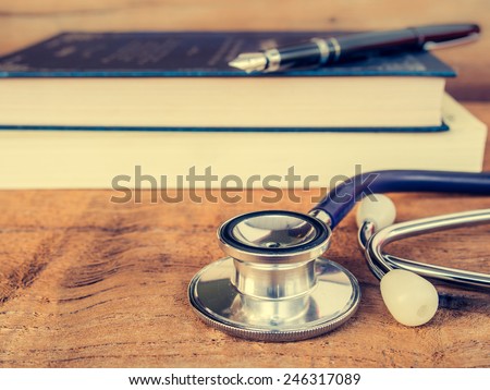 Doctors Stethoscope on wooden background with text book for medical concept in vintage style.