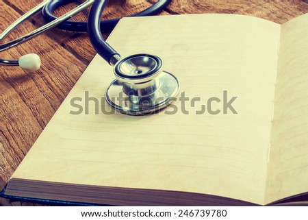 Doctors Stethoscope on a blank notepad with wooden plate for medical concept  in vintage style.