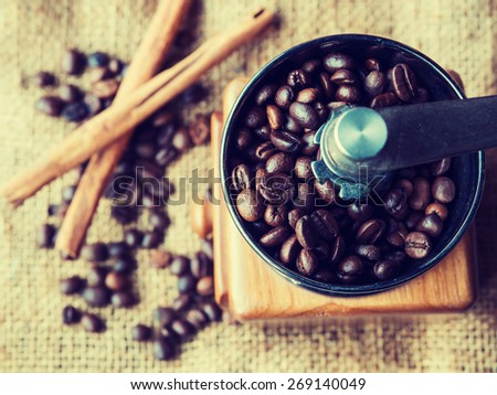 Vintage style photo of the roasted coffee beans in a coffee grinder with blur cinnamon and coffee beans background.
