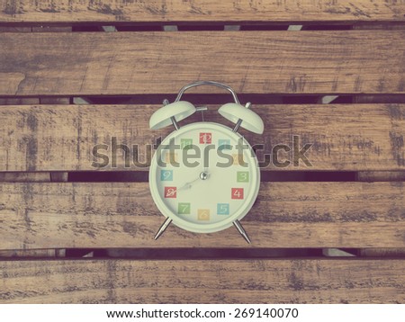 The  white retro alarm clock with colorful number is showing 8 o'clock on wooden background in vintage style.
