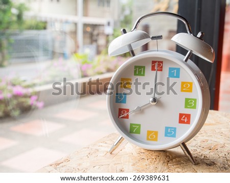 The  white retro alarm clock with colorful number is showing 8 o'clock on wooden background and window glass