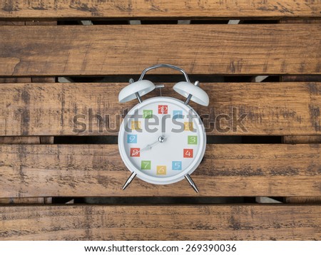 The  white retro alarm clock with colorful number is showing 8 o'clock on wooden background