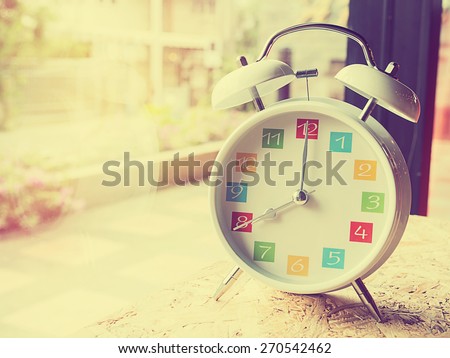 The  white retro alarm clock with colorful number is showing 8 o\'clock on wooden background and window glass in vintage style.