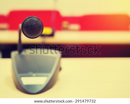 Vintage style photo of the microphone in conference  room or symposium event with de focused meeting room in background. Extremely shallow dof. Filtered process.