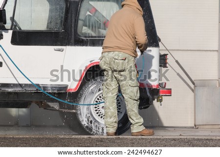 Man washing his car with a jet of water and shampoo