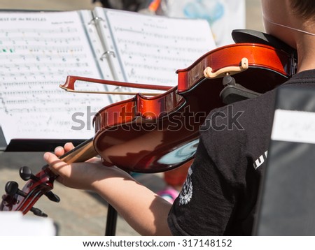 Little Violinist with white Hat during Outdoor Concert, Music Sheet in Background