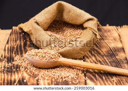 Cloth bag with buckwheat groats and wooden spoon  on wooden background