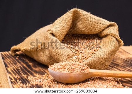 Cloth bag with buckwheat groats and wooden spoon  on wooden background