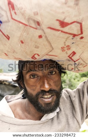 Gowindghat, India - August 11, 2010: Unidentified Indian man carrying a large bag on his head. He was employed in carrying on the mountain. /Indian man carrying big bag on his head