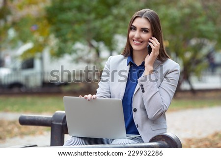 Beautiful business woman talking on the phone with laptop in the park