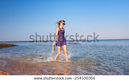 Beautiful girl in lilac dress running on the beach. Sea spray