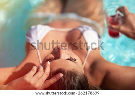 Woman with cocktail relaxing in swimming pool, top view. Woman enjoying sunshine on exotic vacation