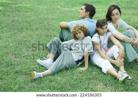Family outdoors, sitting on grass back to back