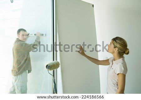 Man holding level against wall and woman putting hand against wall board