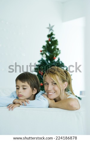 Boy and mother on sofa, Christmas tree in background, woman smiling at camera, boy frowning