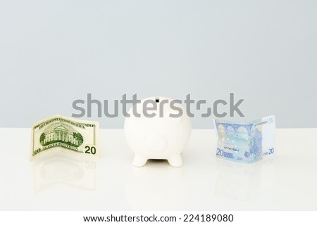 Piggy bank with folded twenty dollar bill to one side and a twenty euro bill on the other side
