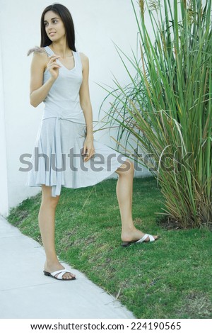 Woman standing by ornamental plant, looking over shoulder, full length portrait