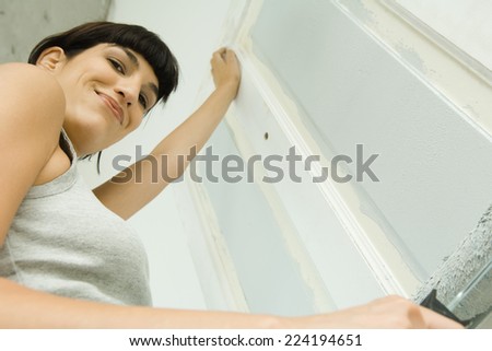 Woman painting door with paint roller, smiling at camera, low angle view