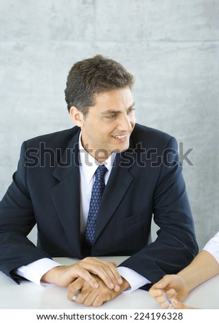 Businessman sitting at table, smiling at colleague