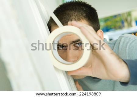 Man putting masking tape on surface, looking through hole