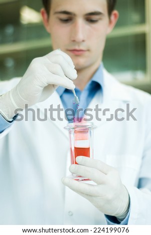 Young male lab worker dipping slide into liquid in beaker
