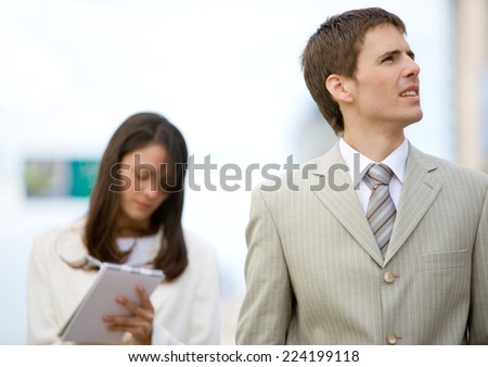 Businessman looking up while female assistant takes notes in background