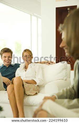 Couple sitting on couch, smiling, friends in foreground