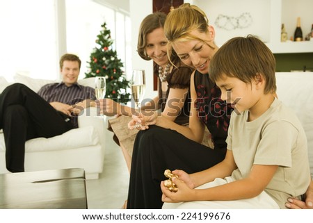 Boy and family sitting on couch, looking at Christmas ornament, Christmas tree in background