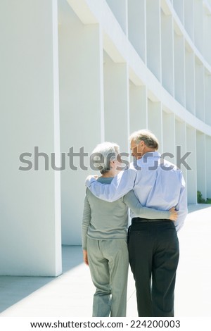 Mature couple walking with arms around each other, rear view