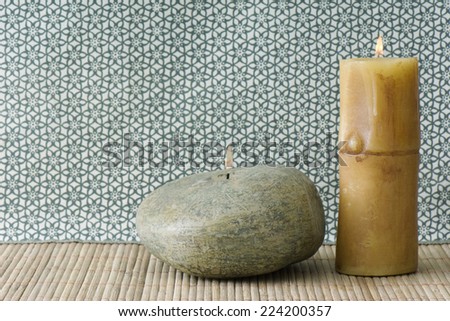 Two candles, one river rock colored and shaped, the other bamboo shaped