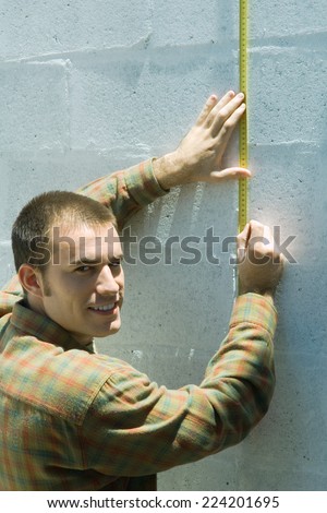 Man measuring wall with measuring tape, smiling over shoulder at camera