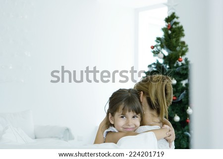 Girl hugging mother by Christmas tree