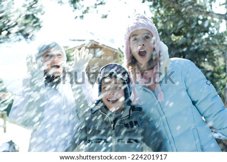 Young friends standing in falling snow, smiling, waist up